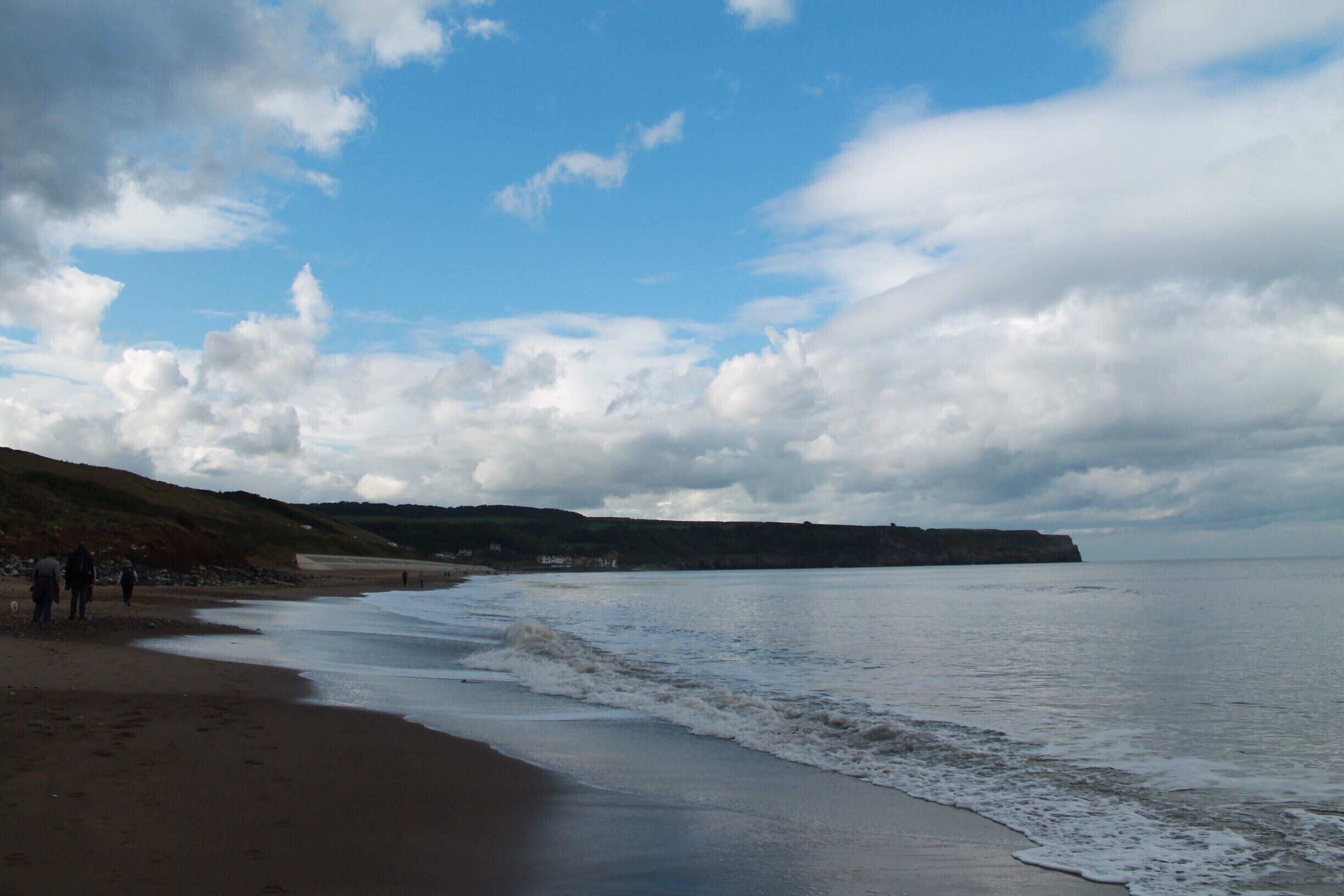 A beach with waves, a clear sky, and a distant cliff.