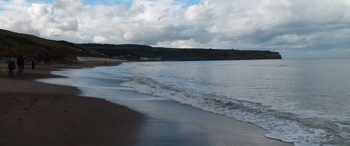 A beach with waves, a clear sky, and a distant cliff.