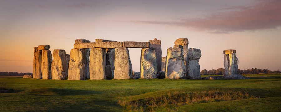 Stonehenge standing in a grassy field with a sunset sky.