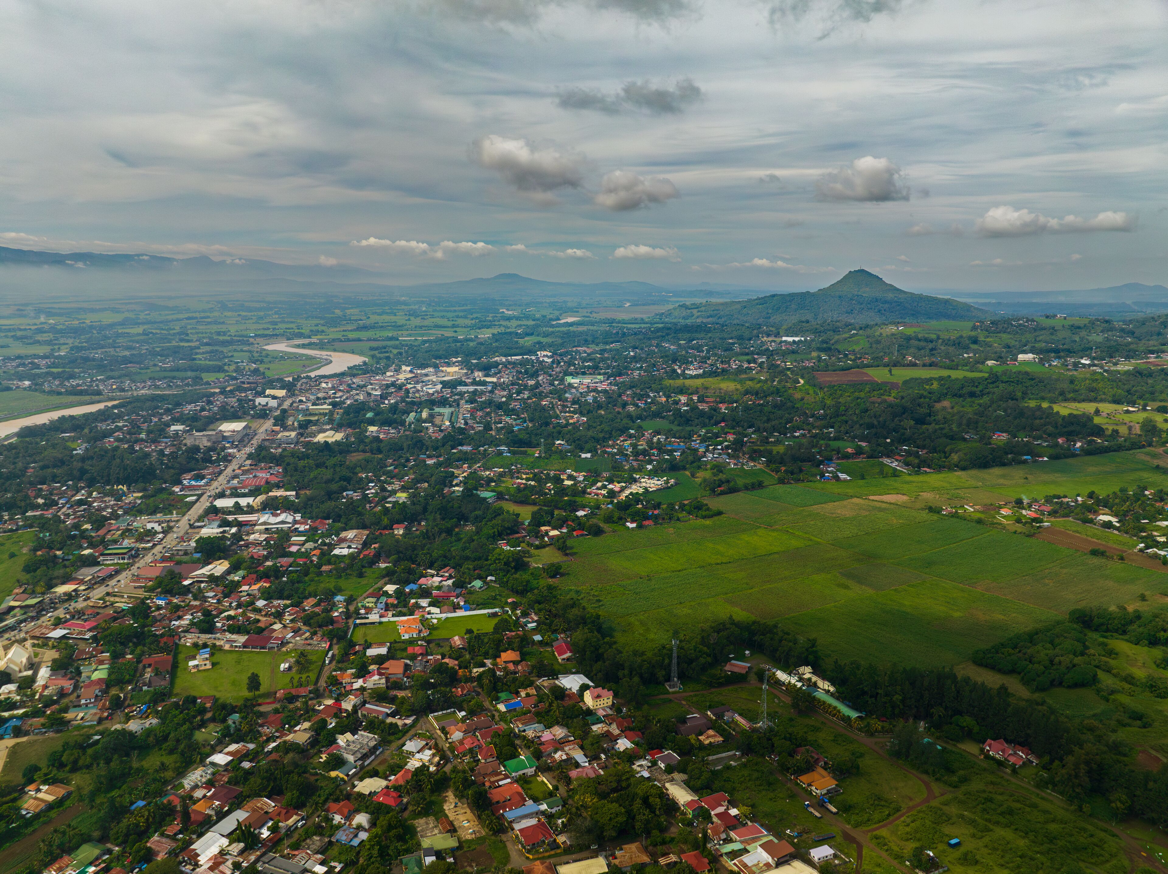 An aerial view of a town with a river, green fields, and a mountain in the background.