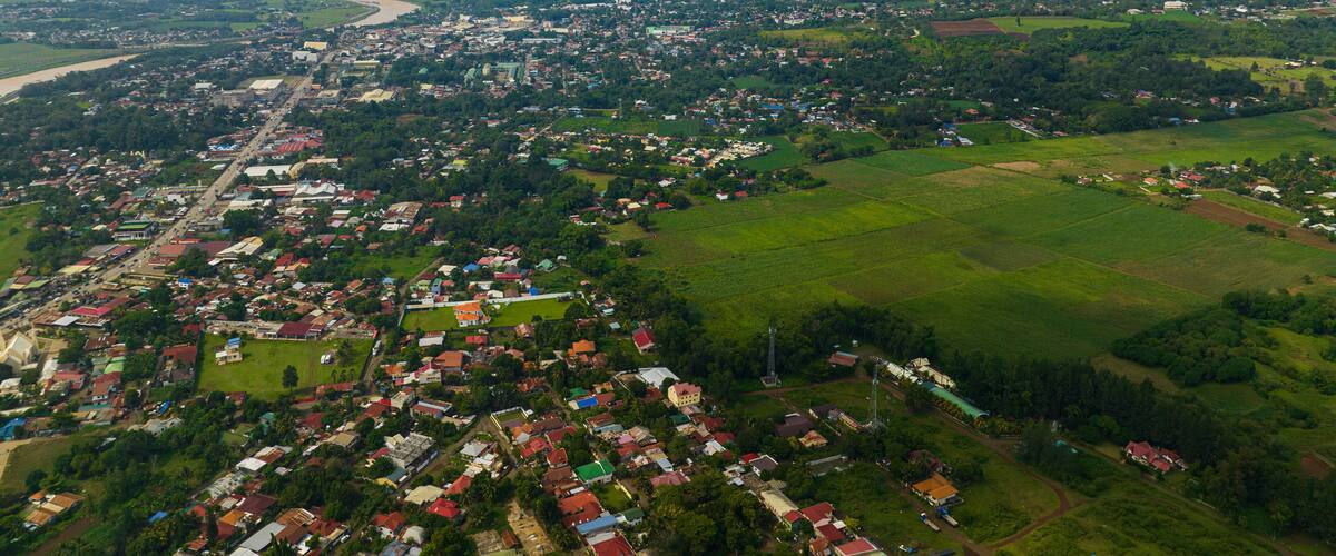 An aerial view of a town with a river, green fields, and a mountain in the background.