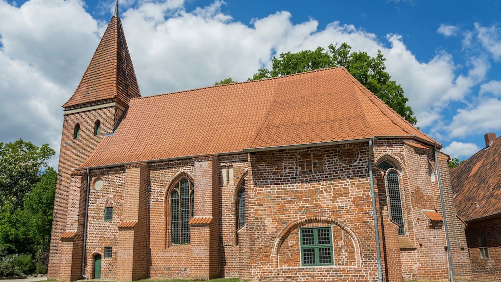 Eine Backsteinkirche mit rotem Ziegeldach und einem hohen Turm.