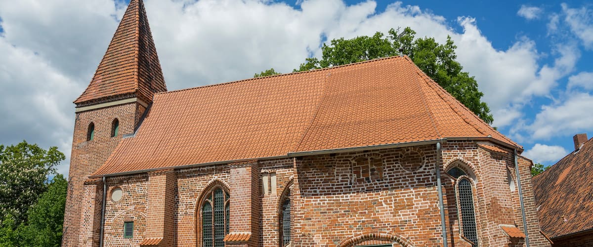 A brick church with a red-tiled roof and a tall tower.