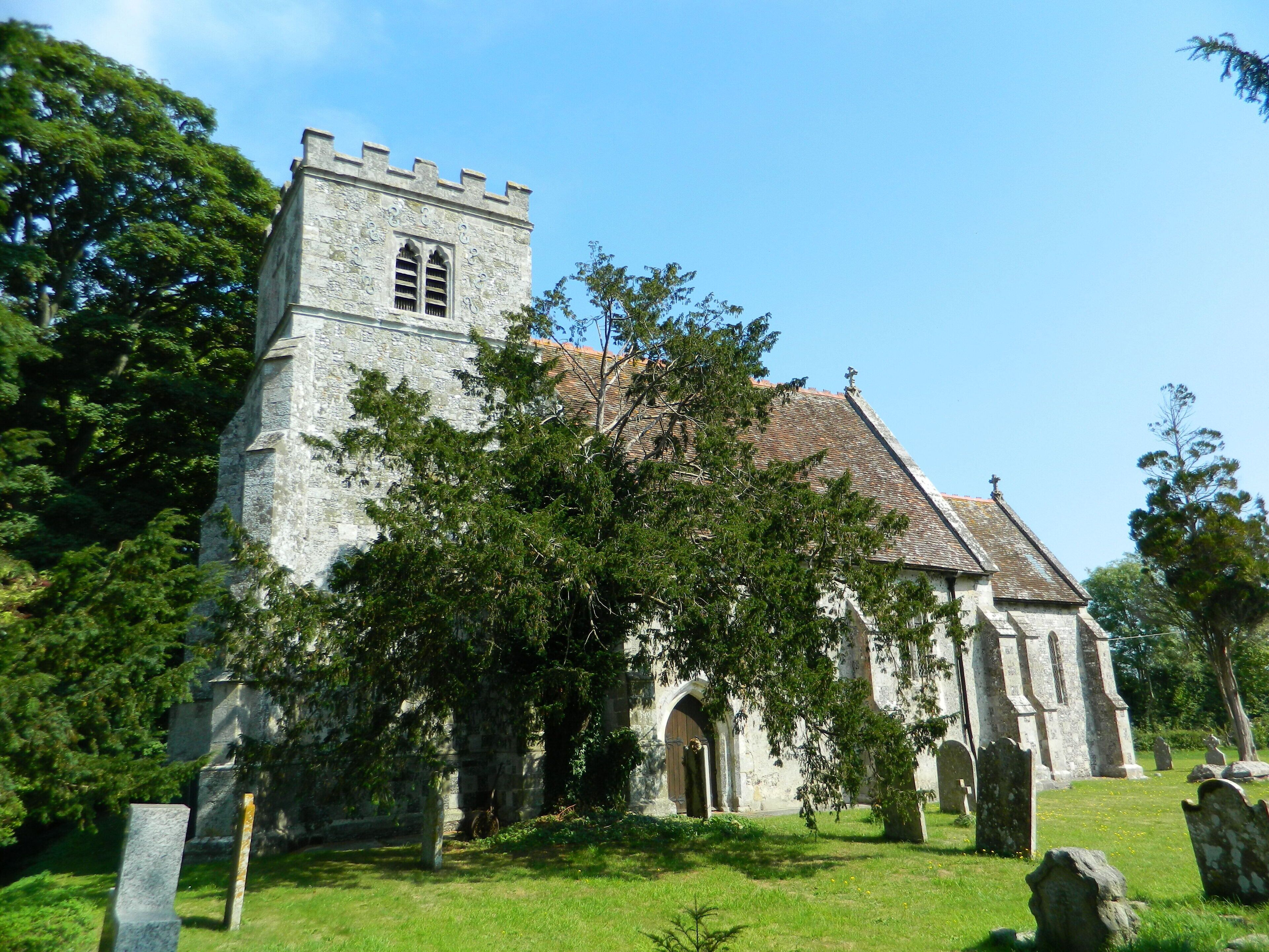 A historic church with a tower and arched doorway, surrounded by trees and gravestones.