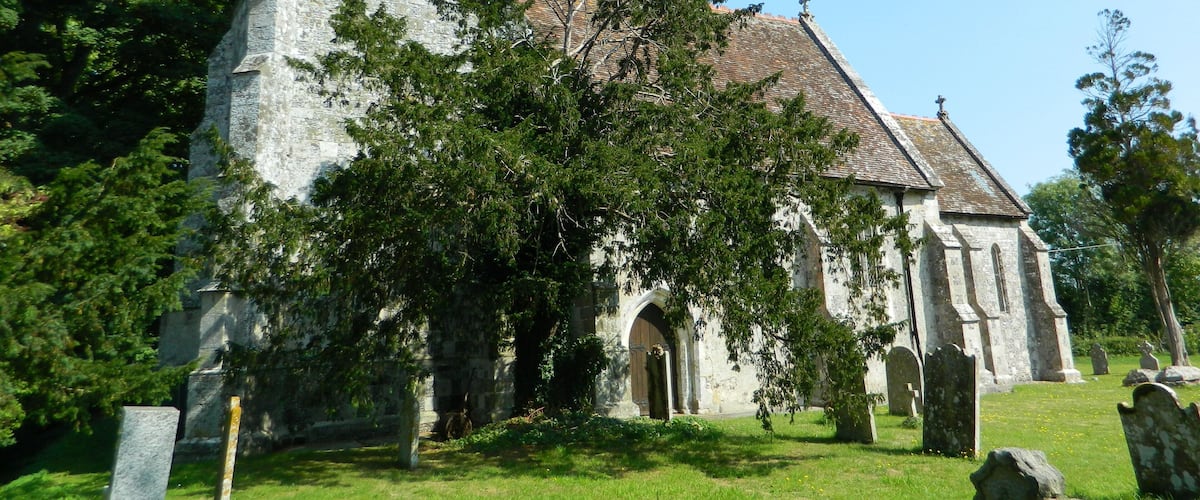 A historic church with a tower and arched doorway, surrounded by trees and gravestones.