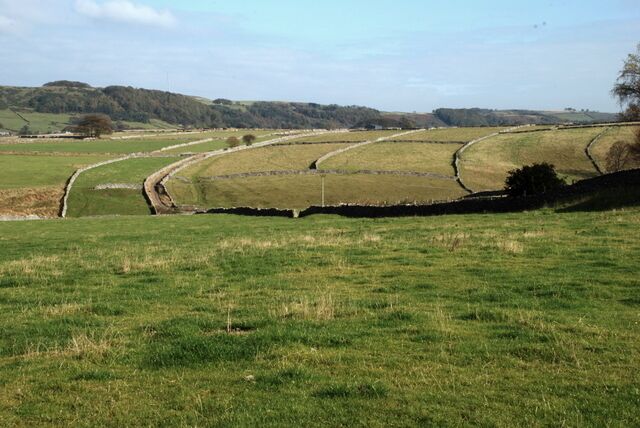 A rural landscape with rolling hills, a narrow water channel, and stone walls.
