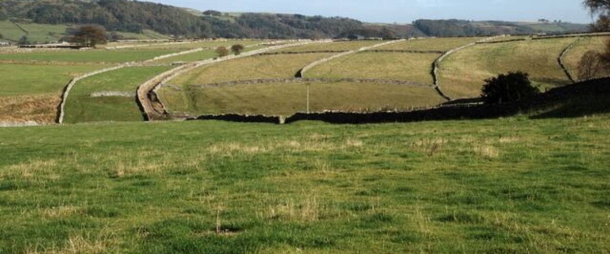 A rural landscape with rolling hills, a narrow water channel, and stone walls.