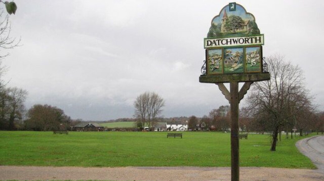 Datchworth Green: The village sign Looking down towards the pavilion the village sign is at the eastern end of the green and has an unusual bas-relief design featuring the church at the top, a rugby match lower left, children playing on a swing and a slide in the middle bottom, and a cricket match lower right. A small plaque on the sign reads:- To the village For the village From the village 2000 indicating that the sign was a Millennium gift.