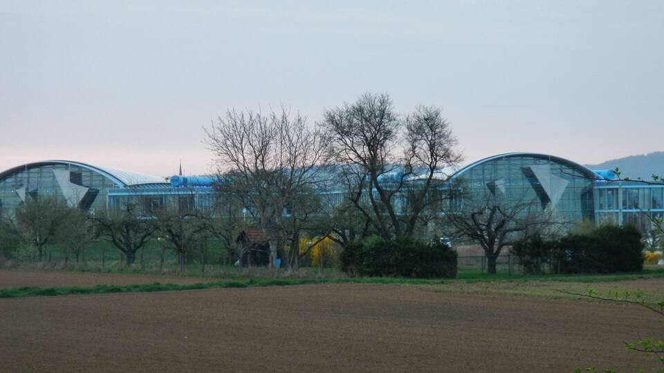 A row of modern, curved-roofed buildings in a rural setting with open fields and leafless trees.