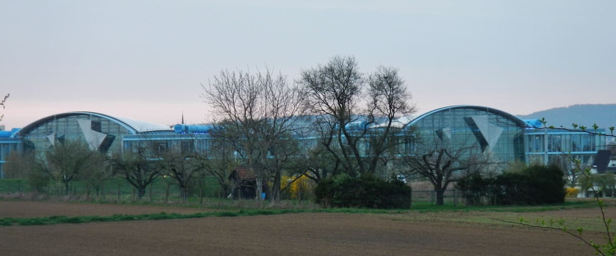 A row of modern, curved-roofed buildings in a rural setting with open fields and leafless trees.