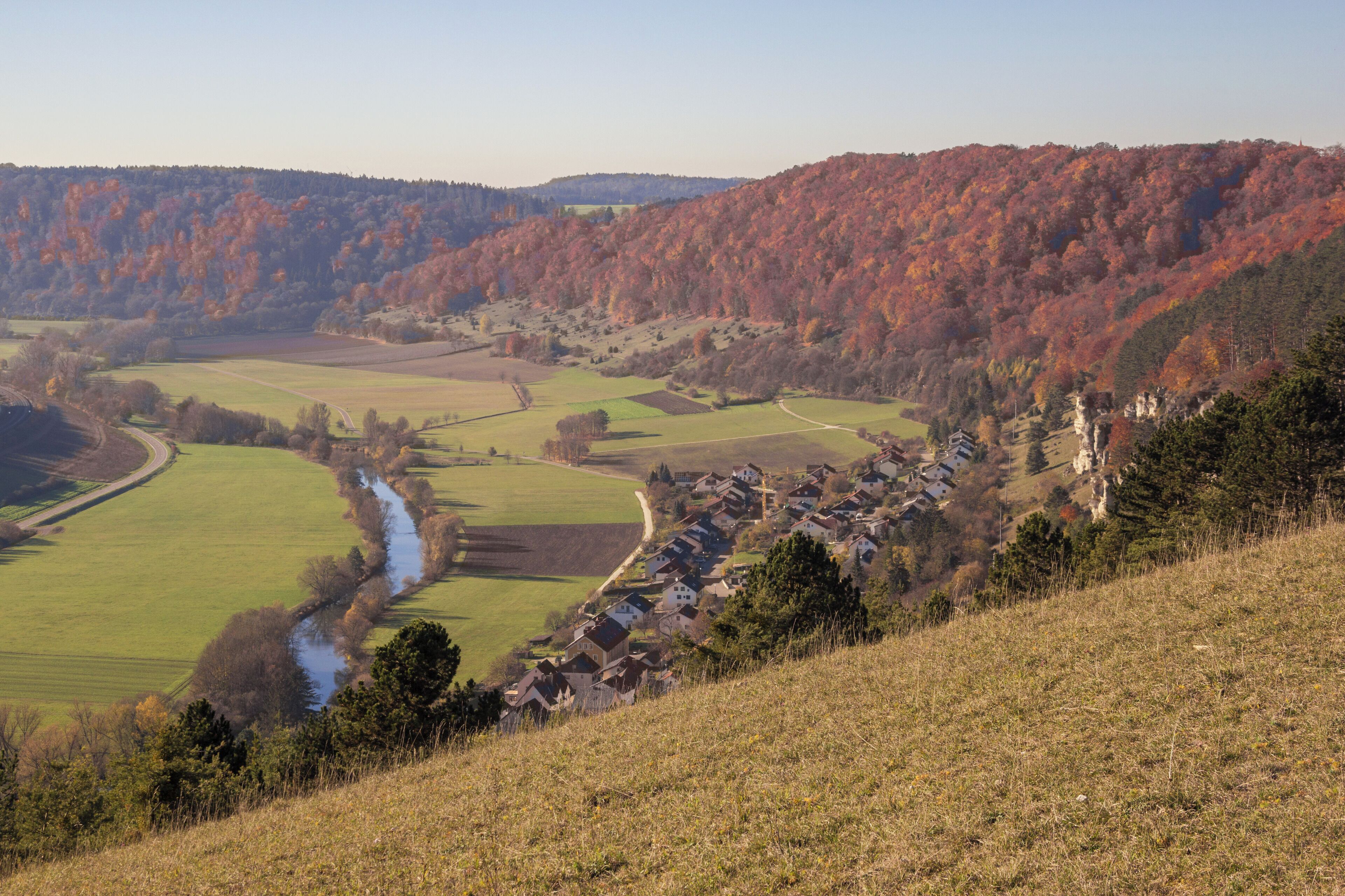 A valley with a river, fields, and a village on a hillside.