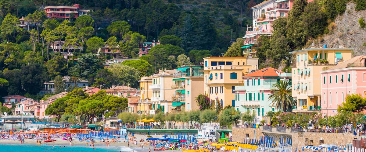 A coastal town with colorful buildings, a beach, and a mountainous backdrop.