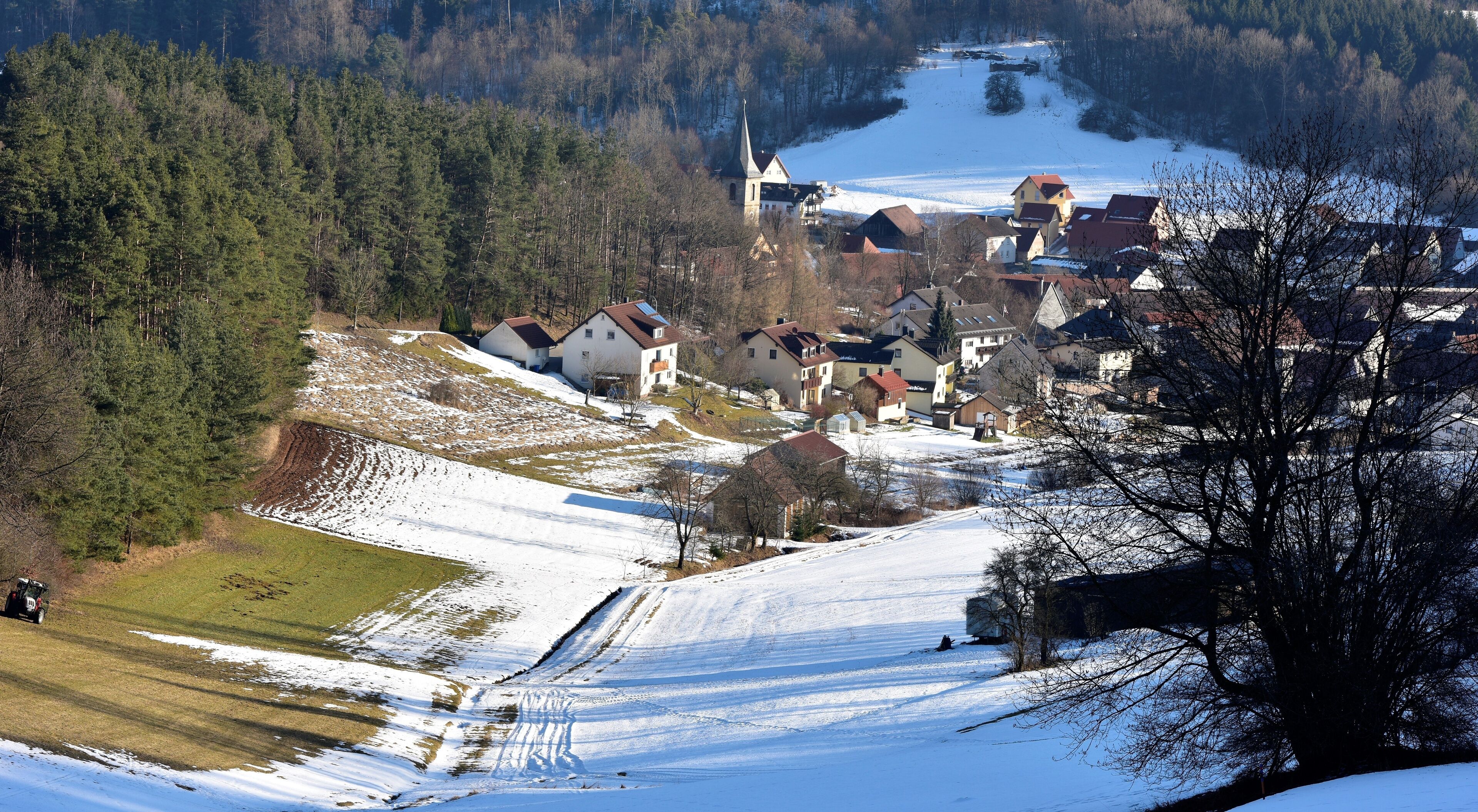 A snow-covered village with houses, a church, and a forested hill.