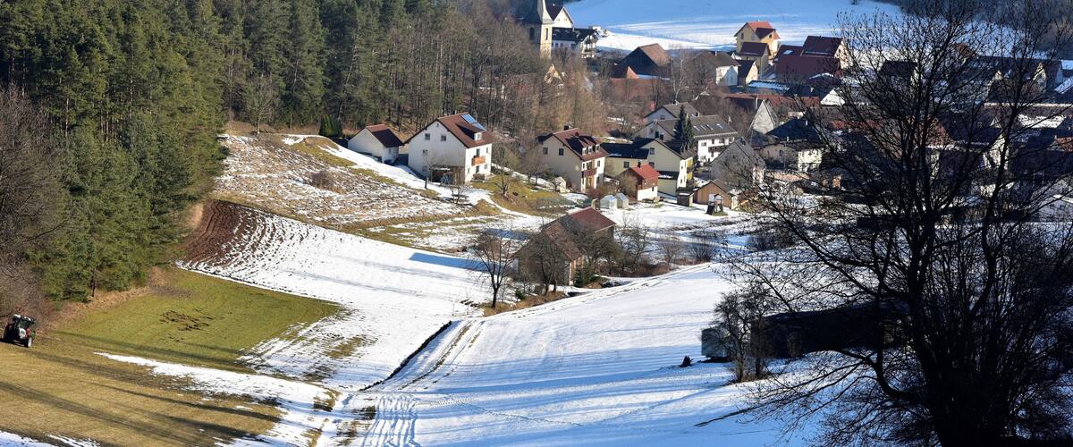 A snow-covered village with houses, a church, and a forested hill.