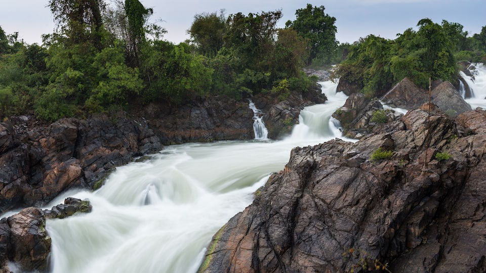 A powerful waterfall cascading over rocky terrain surrounded by dense green foliage.