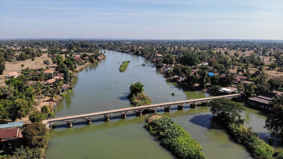A river with a bridge, surrounded by greenery and small buildings.