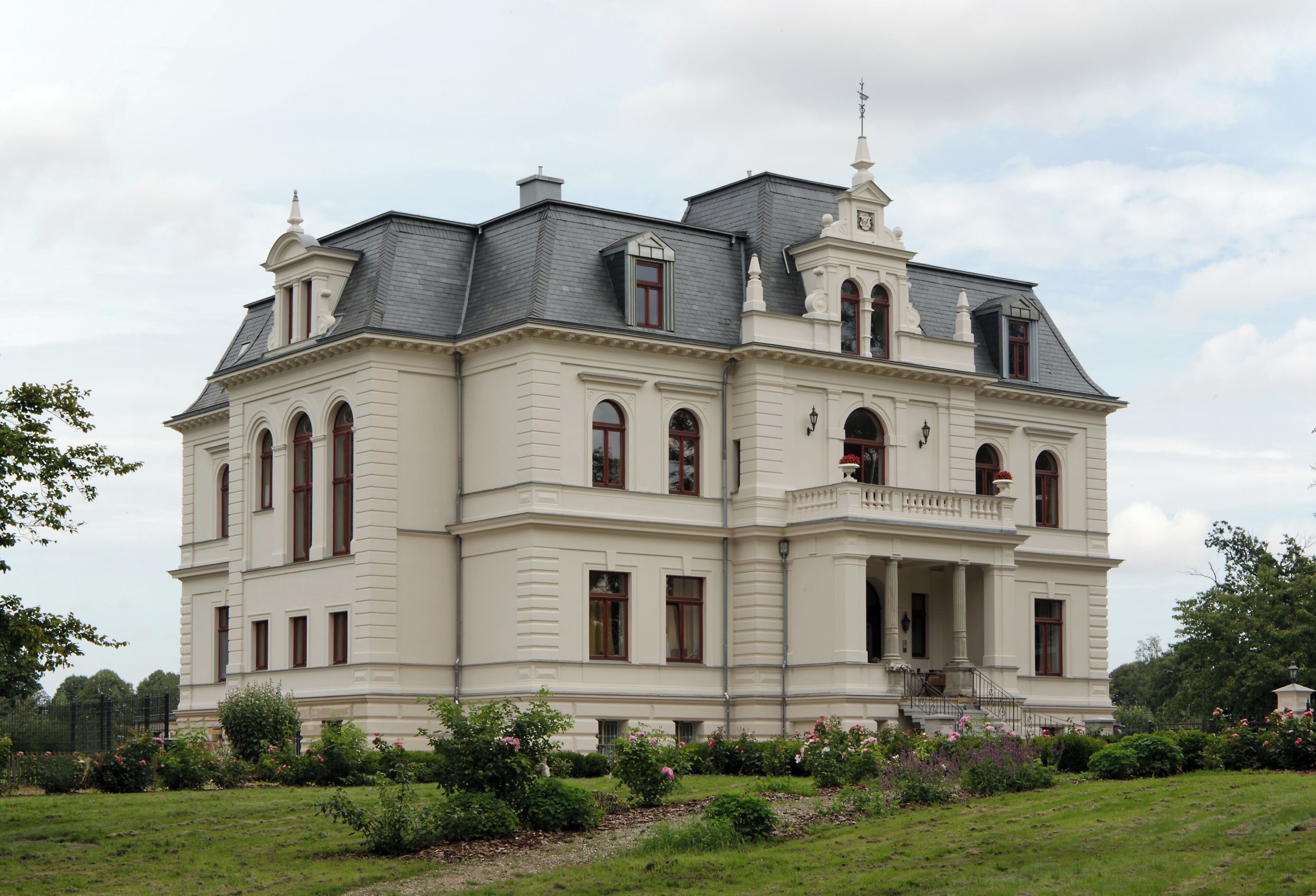 A large, historic building with a symmetrical facade, multiple windows, and a prominent balcony.