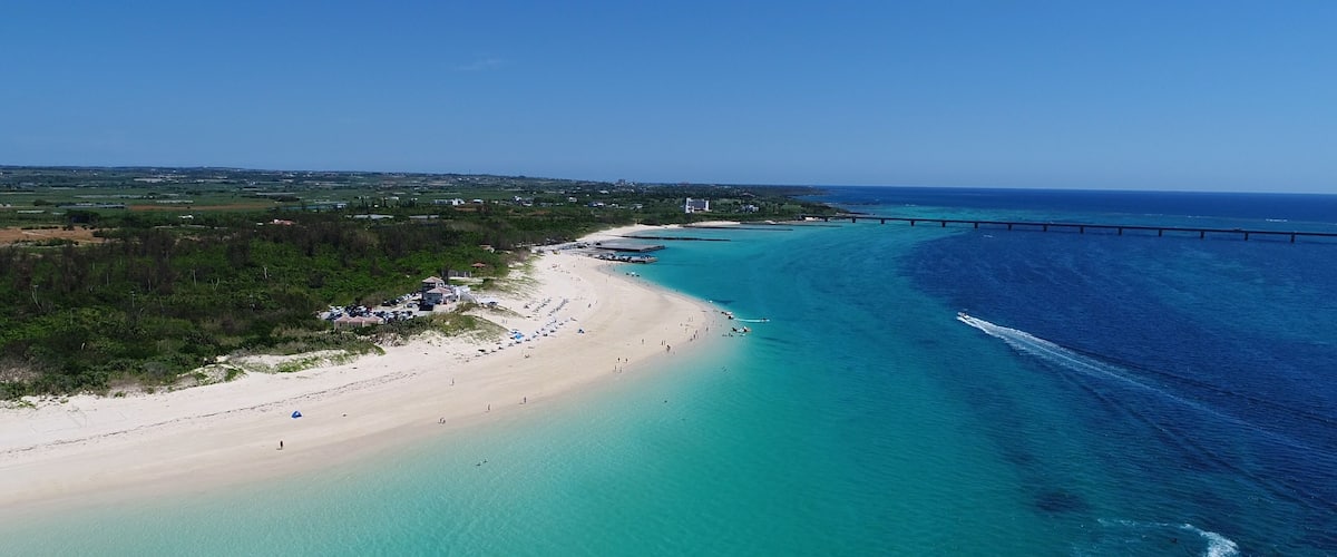 A coastal landscape with a beach, clear turquoise waters, and a bridge.