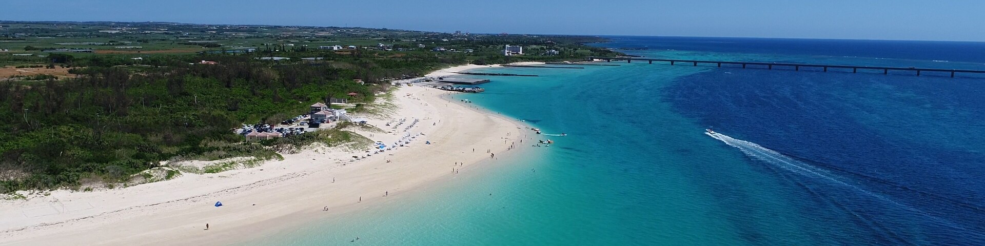 A coastal landscape with a beach, clear turquoise waters, and a bridge.
