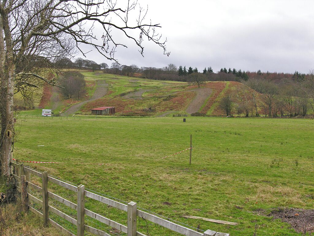 A rural landscape with rolling hills, a wooden fence, and a small red building in the distance.