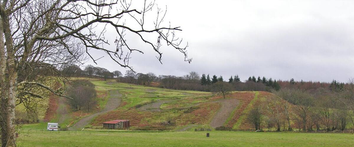 A rural landscape with rolling hills, a wooden fence, and a small red building in the distance.