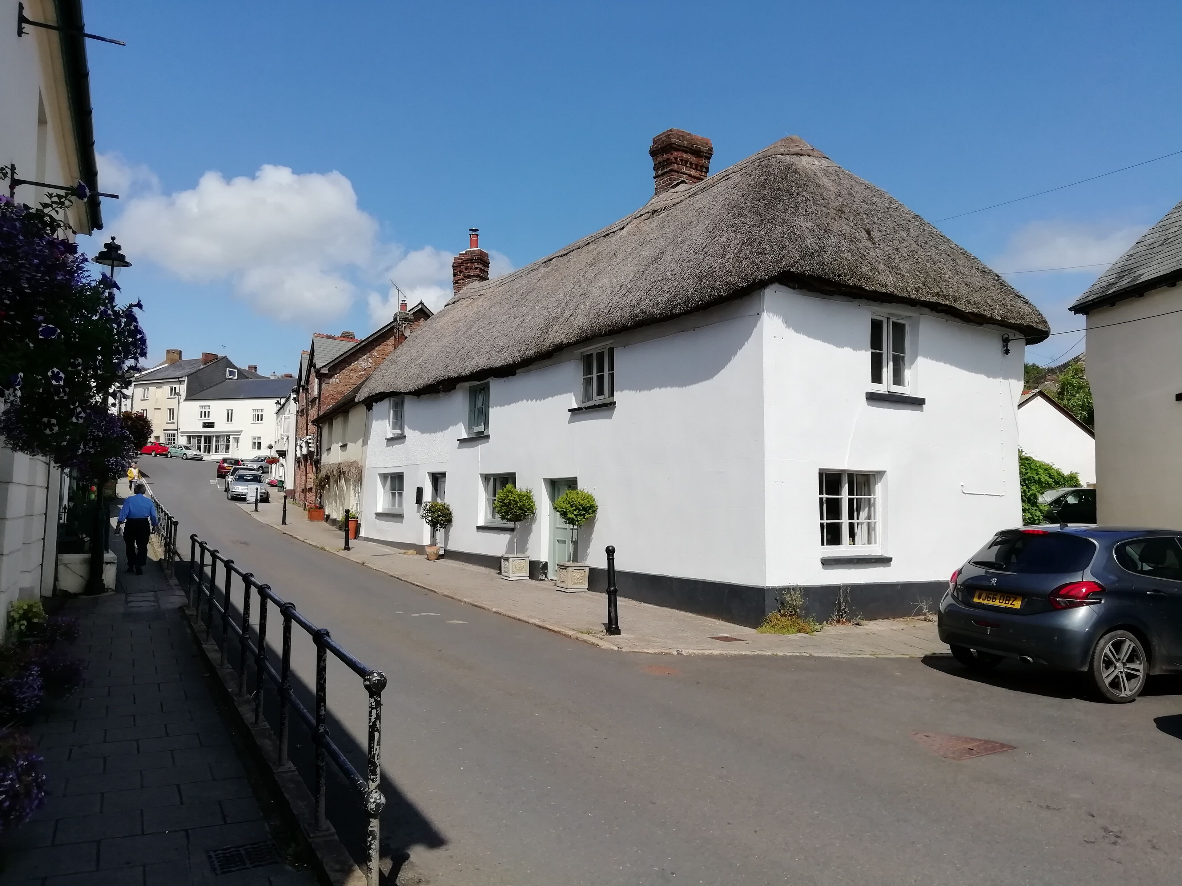 A quaint street with white buildings, thatched roofs, and parked cars.