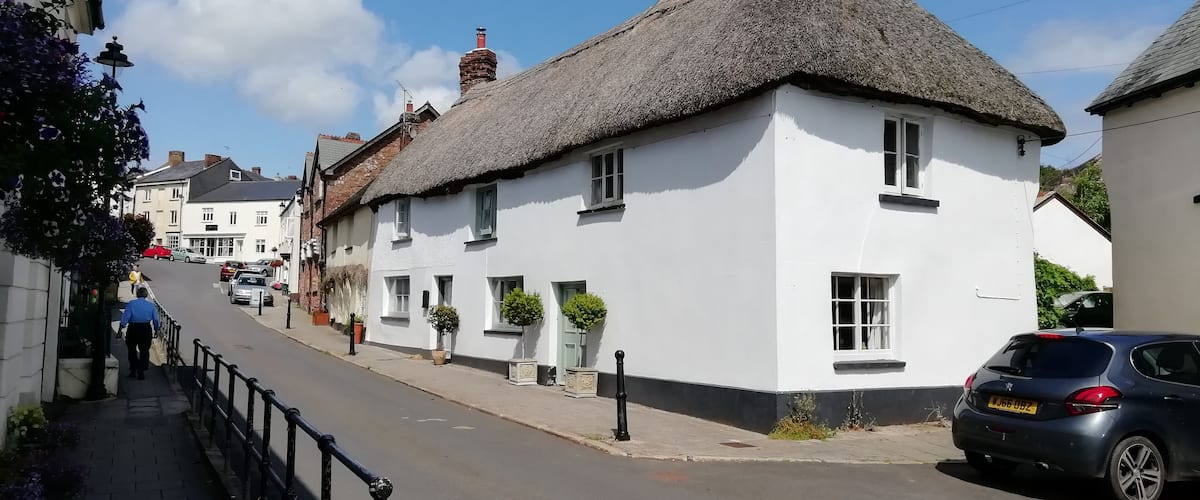 A quaint street with white buildings, thatched roofs, and parked cars.