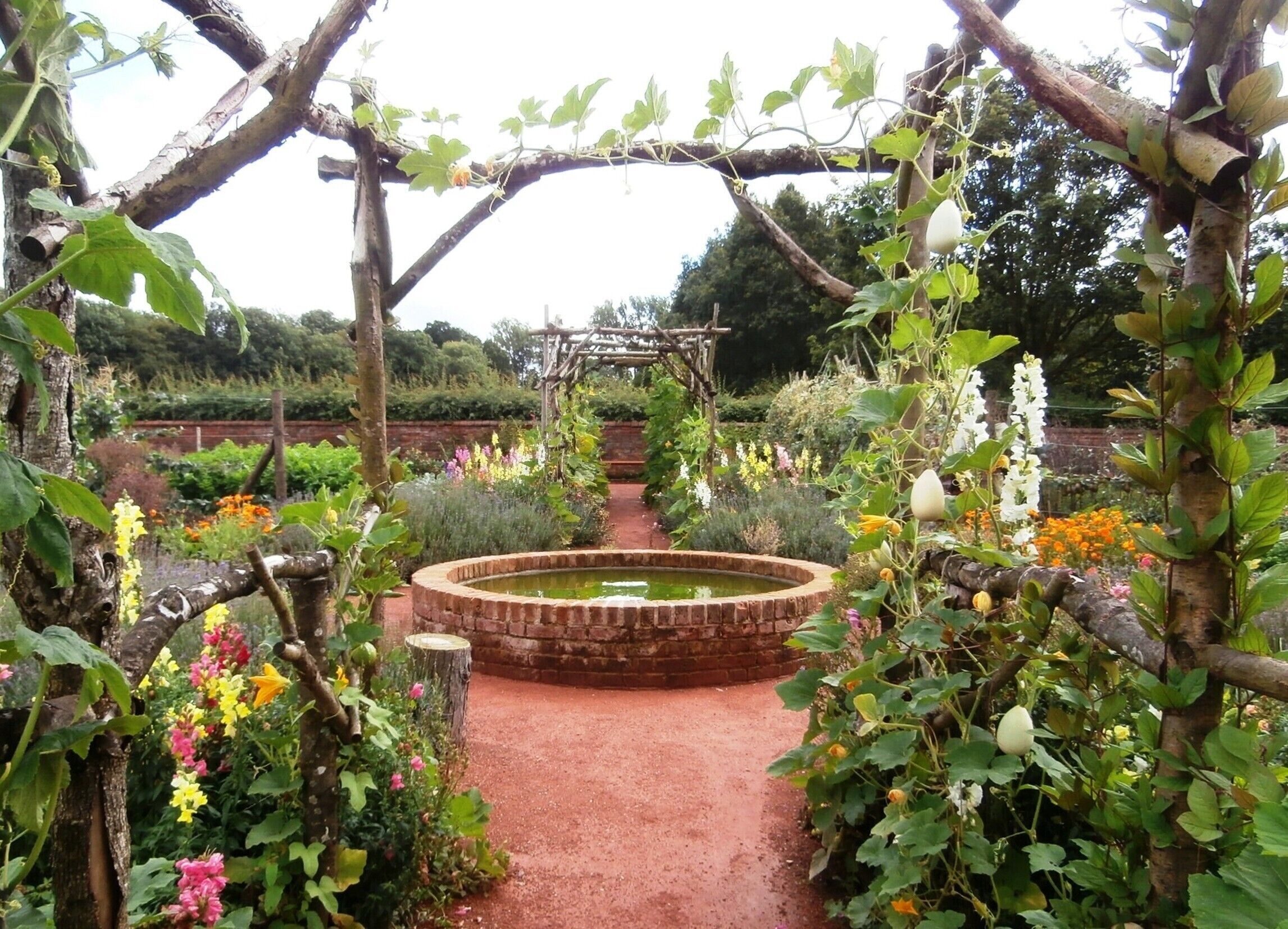 A garden with a brick fountain, flowering plants, and a wooden pergola.