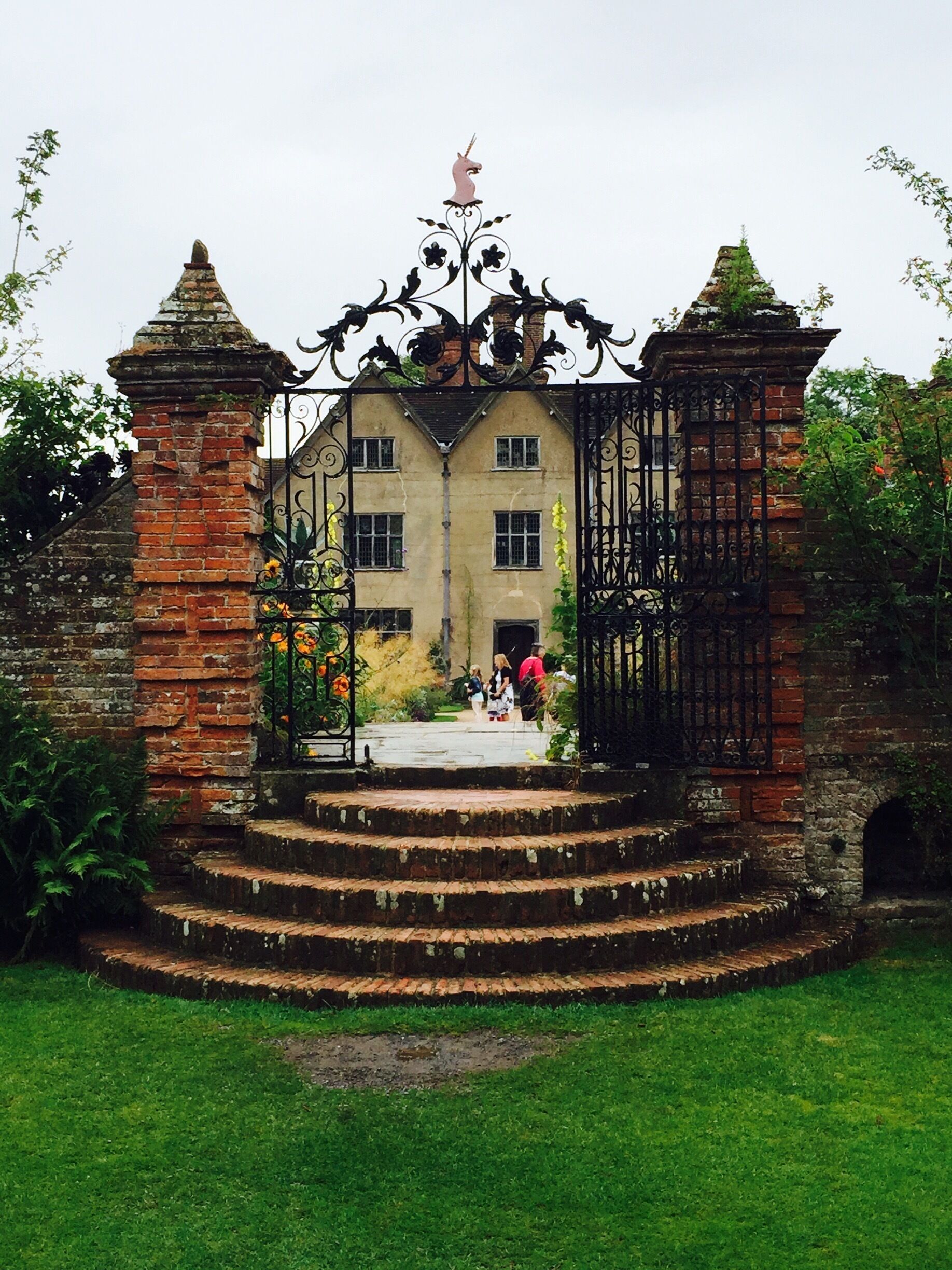 A historic building with a wrought iron gate, brick pillars, and a unicorn statue.