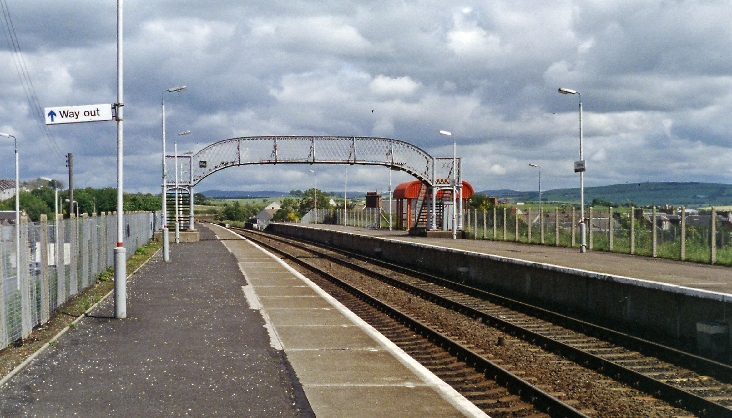 A railway station platform with a 'Way out' sign, tracks, and a fenced area.
