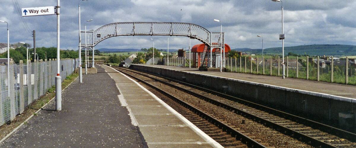 A railway station platform with a 'Way out' sign, tracks, and a fenced area.