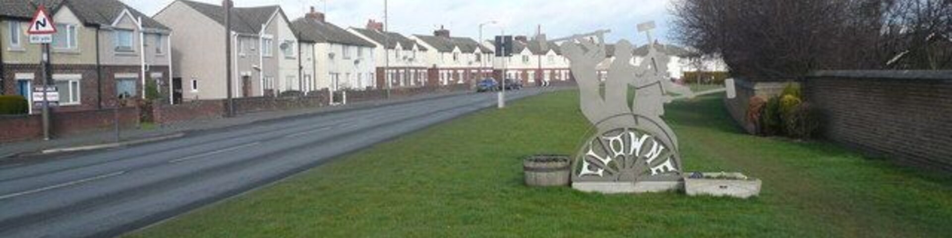 Rua residencial com casas, uma placa de sinalização e uma grande escultura de metal.