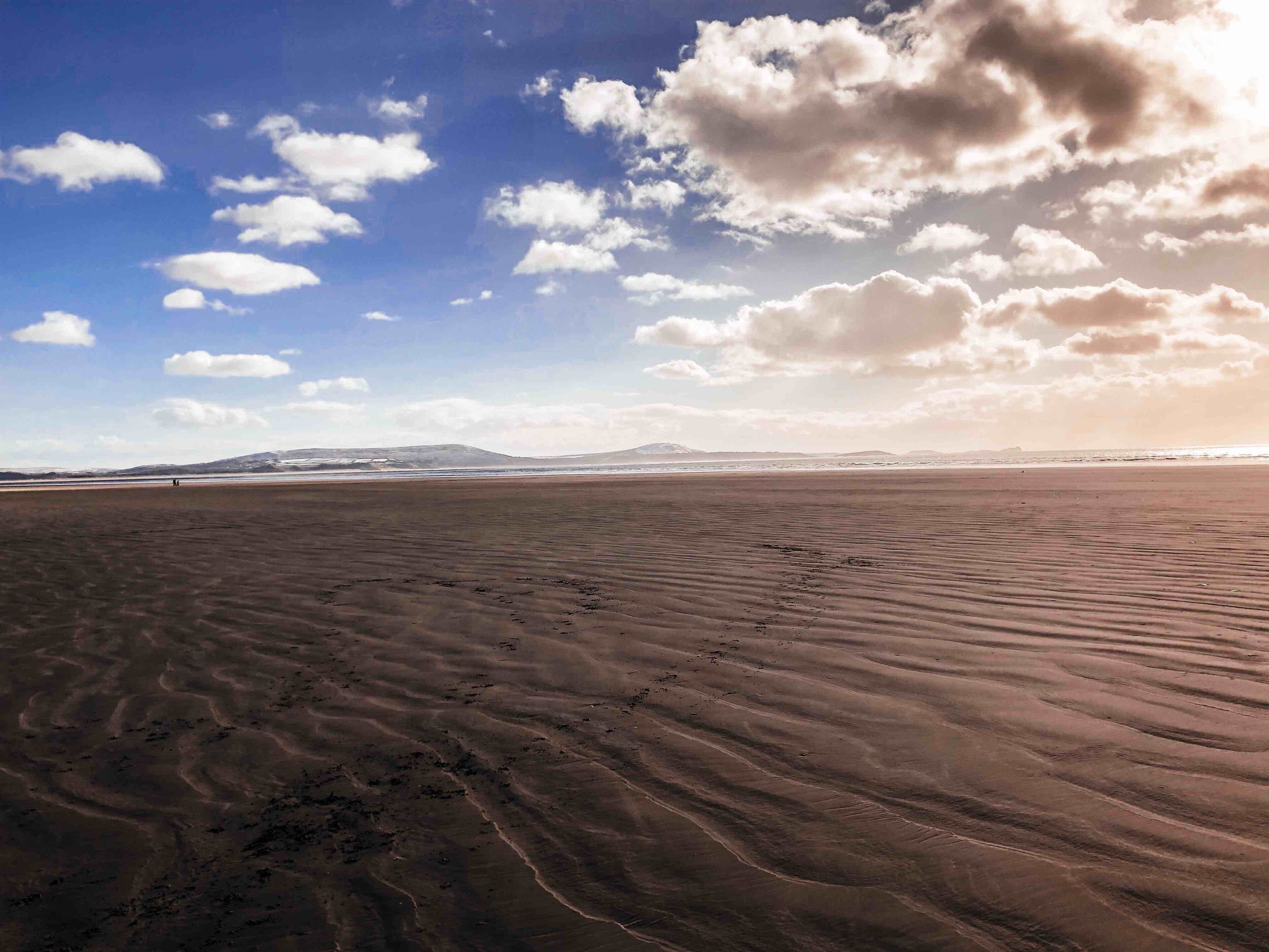 A vast desert landscape with rippled sand dunes under a partly cloudy sky.