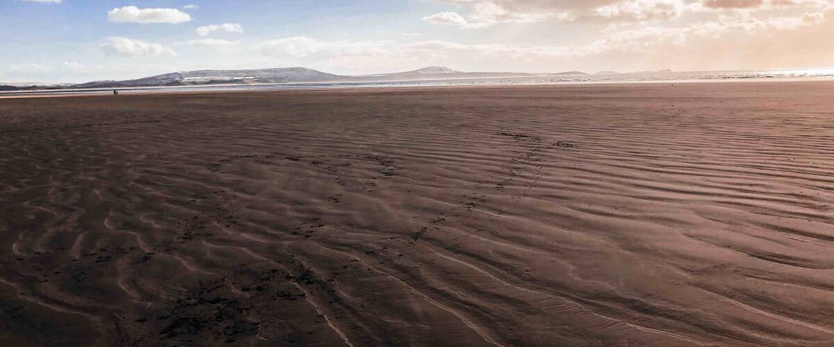 A vast desert landscape with rippled sand dunes under a partly cloudy sky.