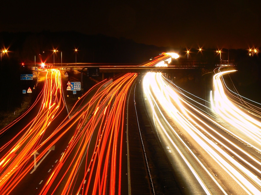 A multi-lane highway at night with light trails from vehicles.