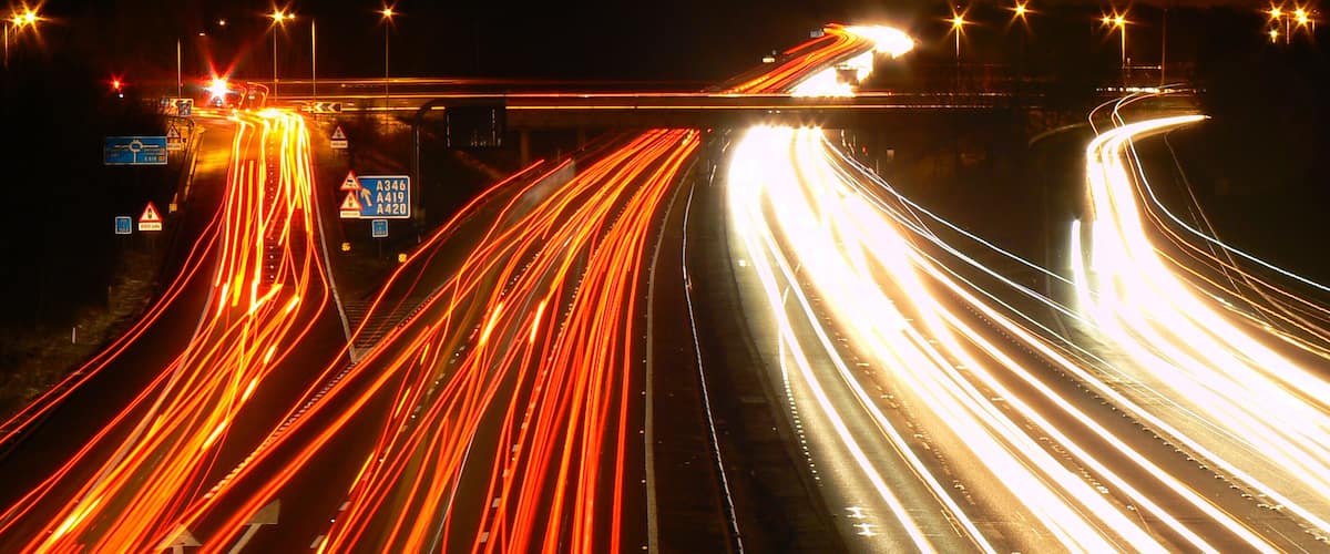 A multi-lane highway at night with light trails from vehicles.