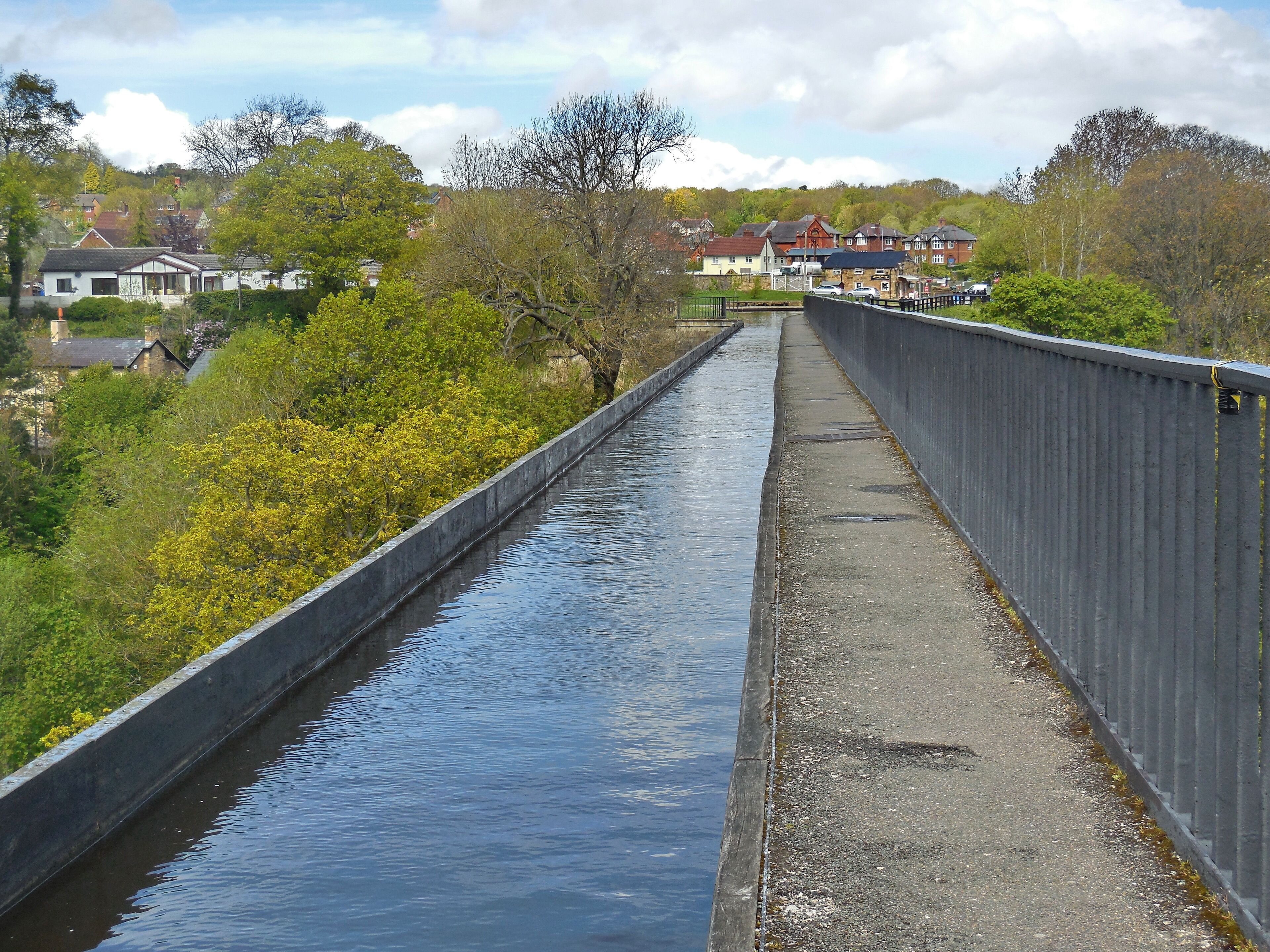 A bridge over a calm river with houses and trees in the background.