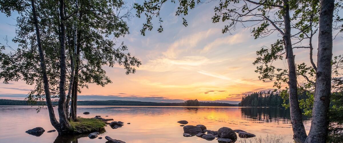 A calm lake with trees reflecting the sunset, surrounded by a forest.