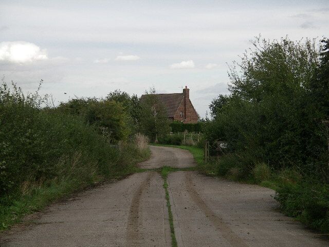 A narrow rural road leading to a house with a red roof.