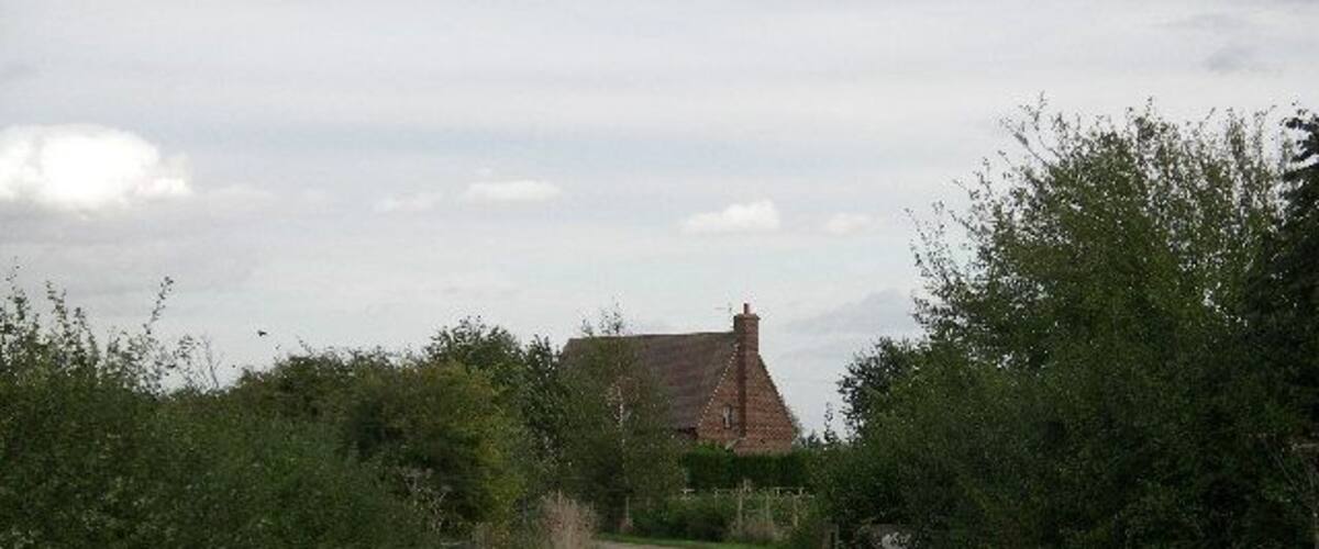 A narrow rural road leading to a house with a red roof.