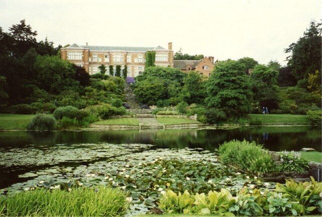 A large building surrounded by lush greenery and a pond with lily pads.