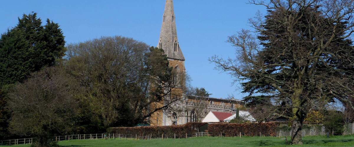 A church with a tall spire, surrounded by trees and a grassy field.