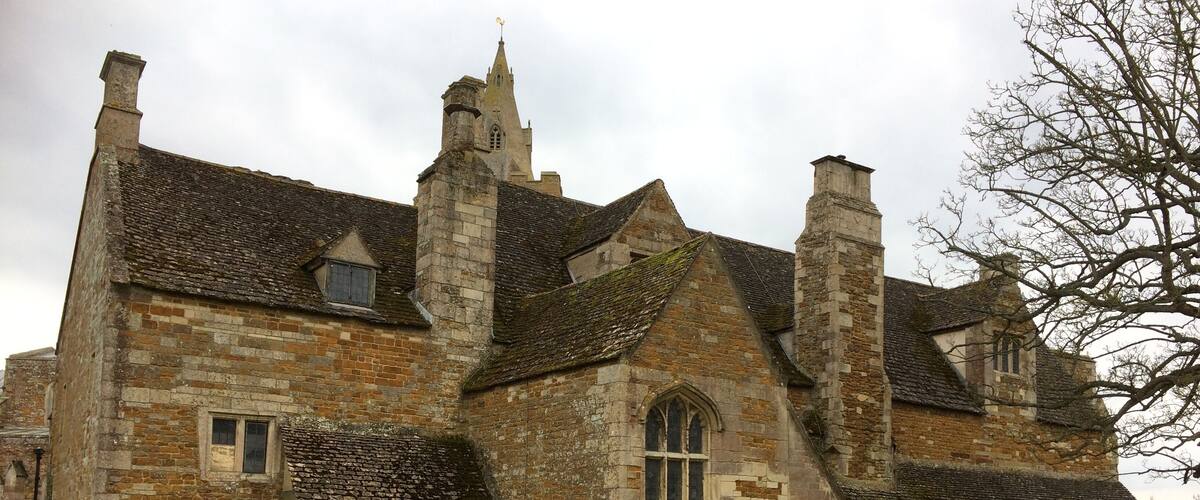 A historic stone building with multiple chimneys and a large lawn in front.