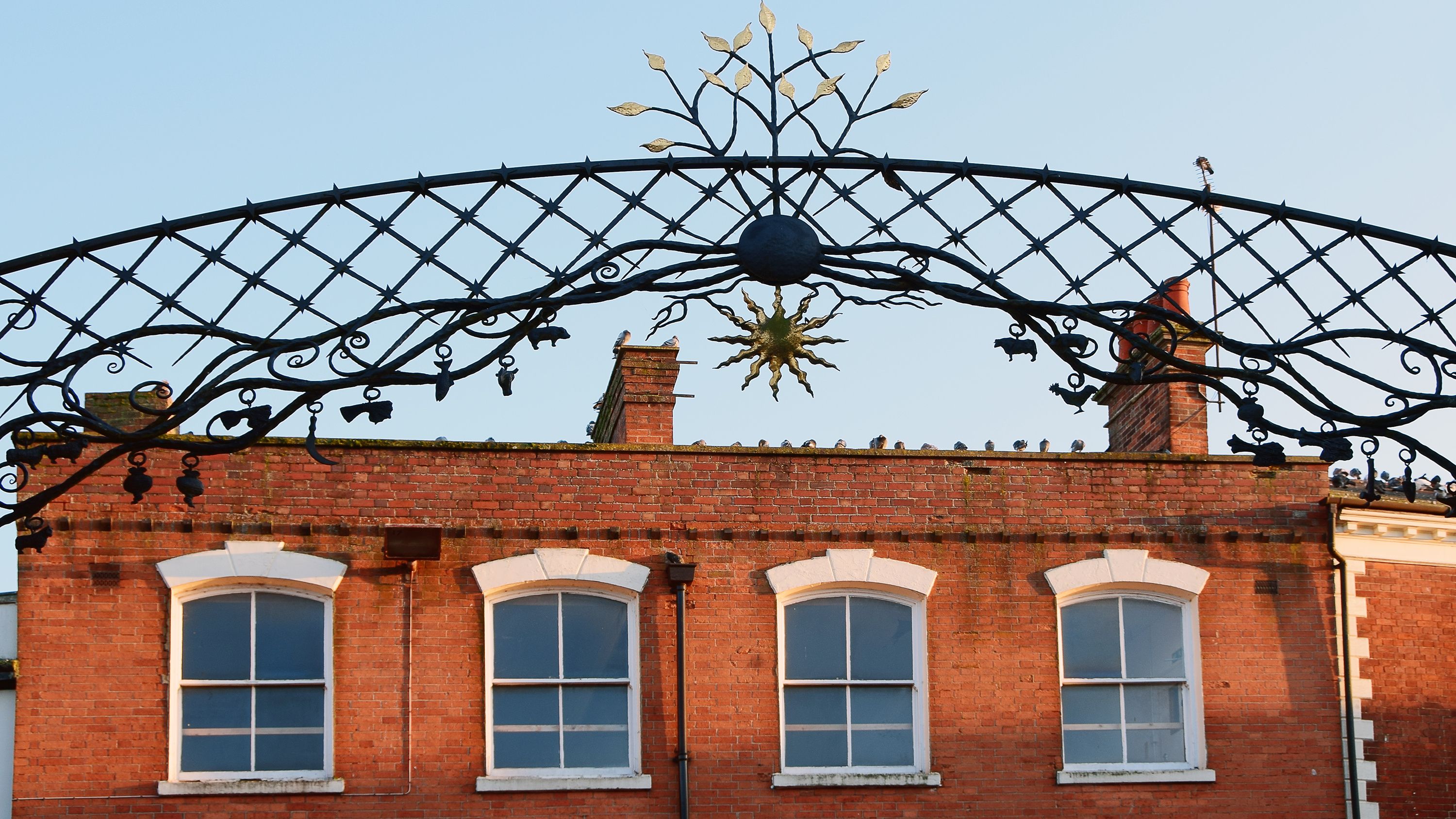 A brick building with arched windows and a decorative metal archway above.