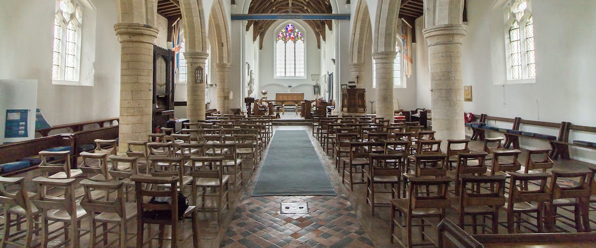 A church interior with wooden pews, stone columns, and a central aisle leading to an altar.