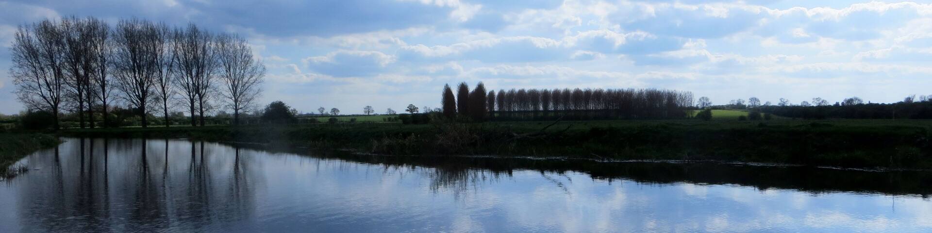 A calm lake reflecting trees and a cloudy sky.