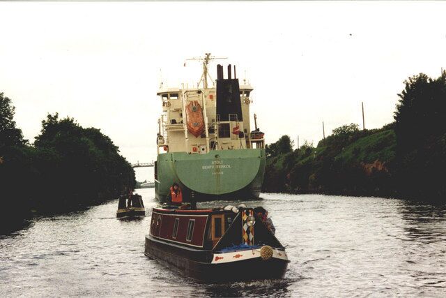 A large green ship on a narrow waterway with a smaller boat nearby.