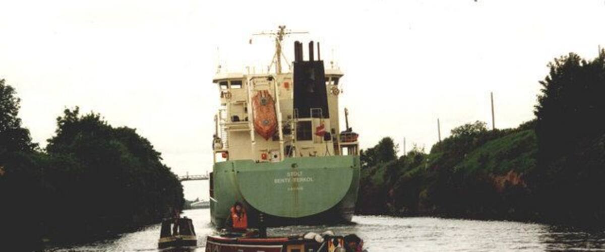 A large green ship on a narrow waterway with a smaller boat nearby.