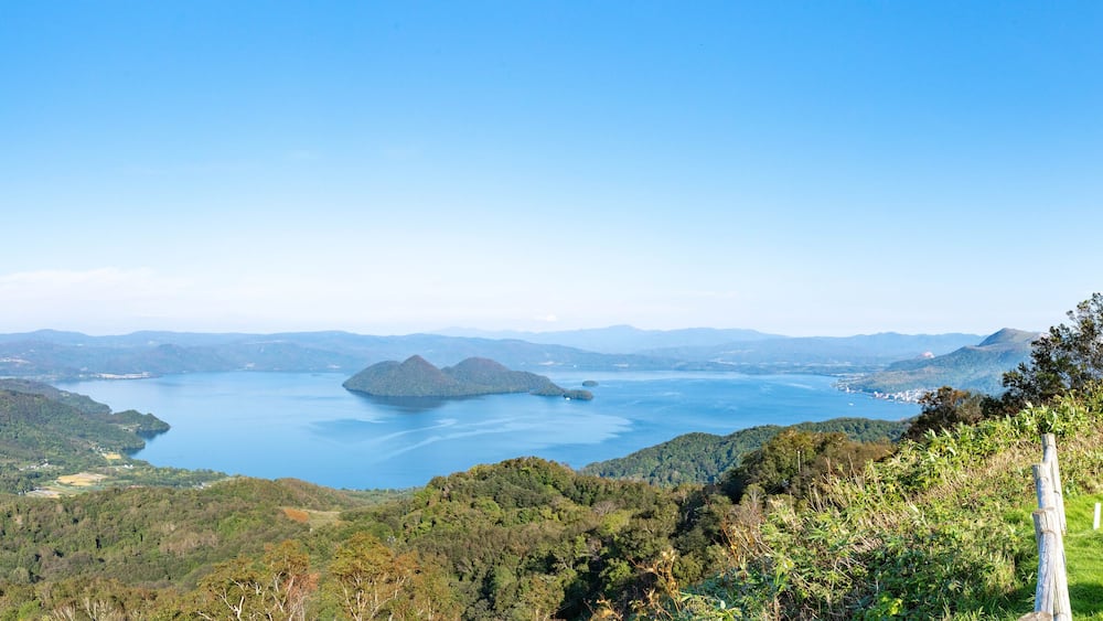 Un paysage montagneux avec un grand lac, entouré de forêts denses et de collines lointaines.