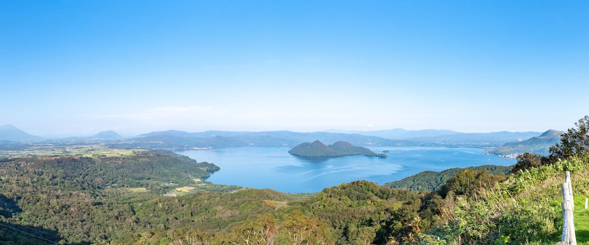 A mountainous landscape with a large lake surrounded by dense forests and distant hills.